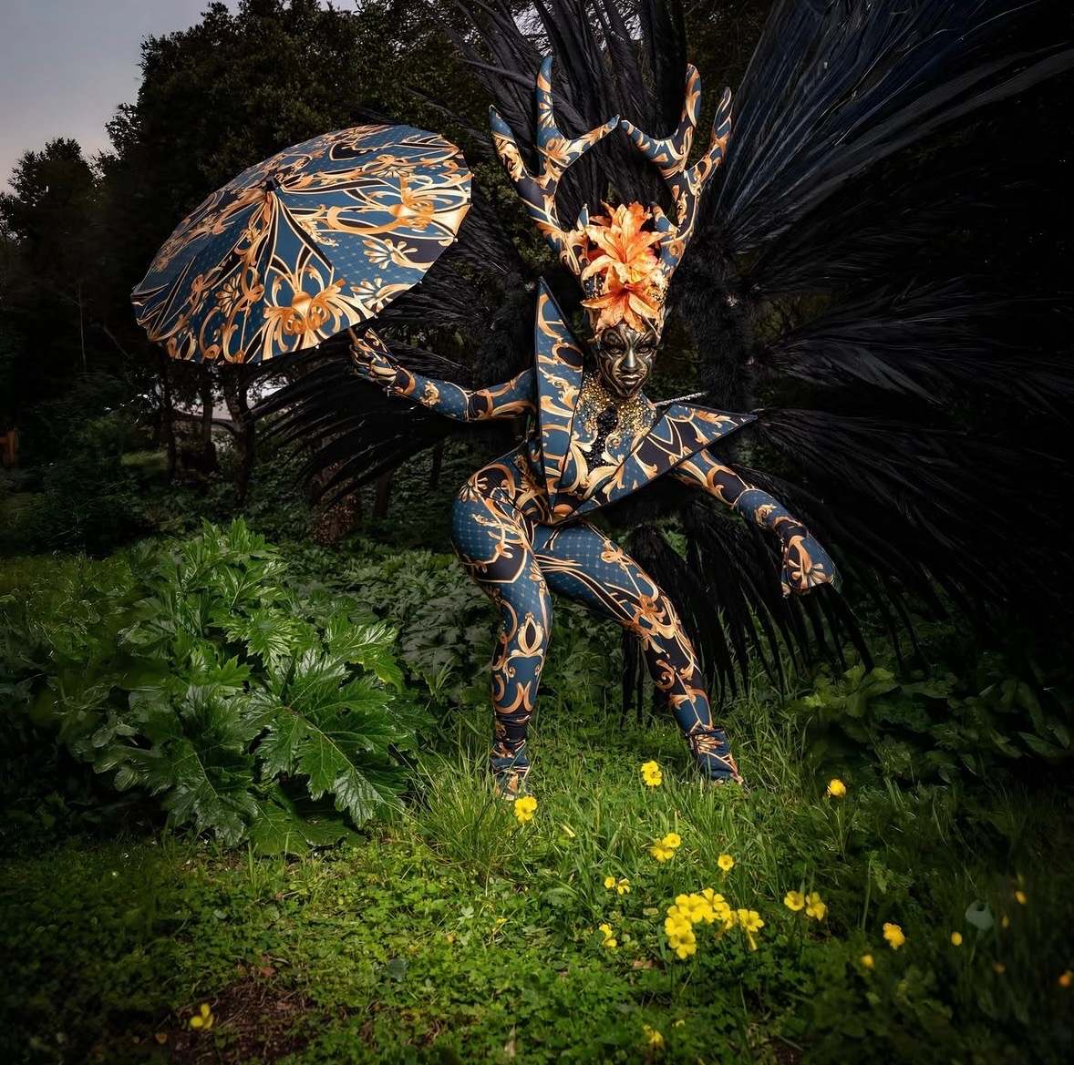Créature ailée bleu et or tenant une ombrelle peinte, dans un jardin