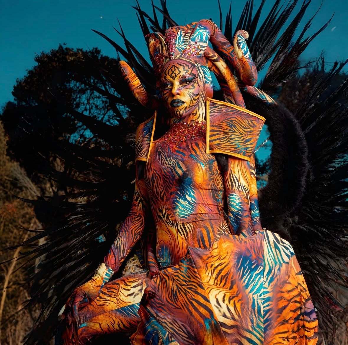 Créature aux motifs tigrés orange et bleu, ailes de plumes noires déployées