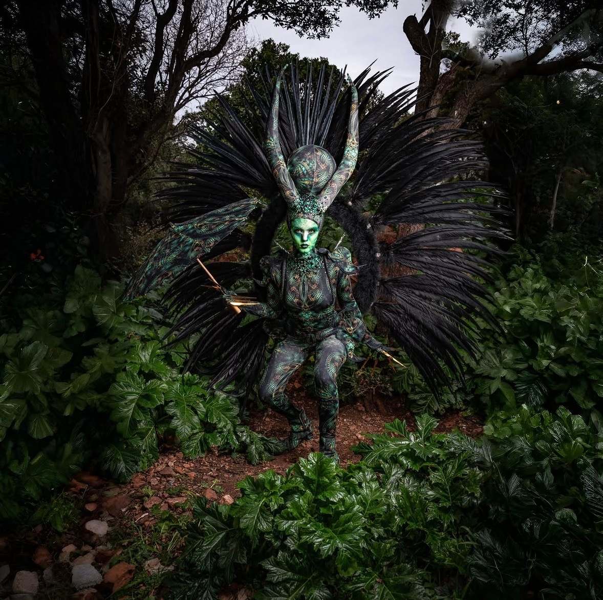 Créature verte casquée devant une grande roue de plumes noires