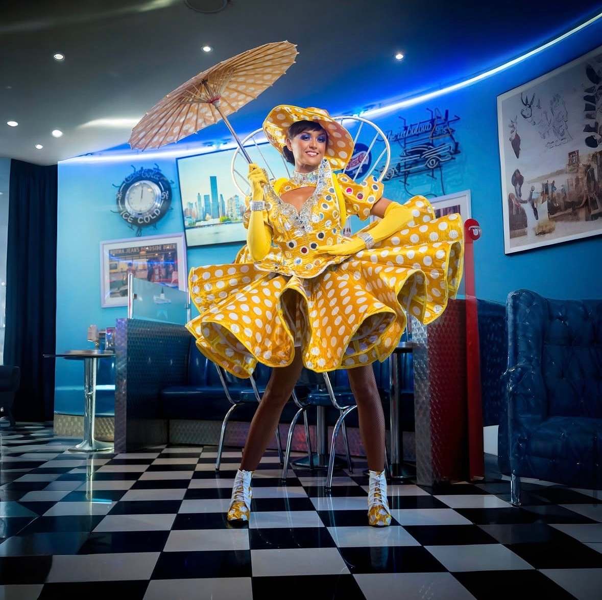 Artiste en robe à pois jaune tenant une ombrelle, sol en damier